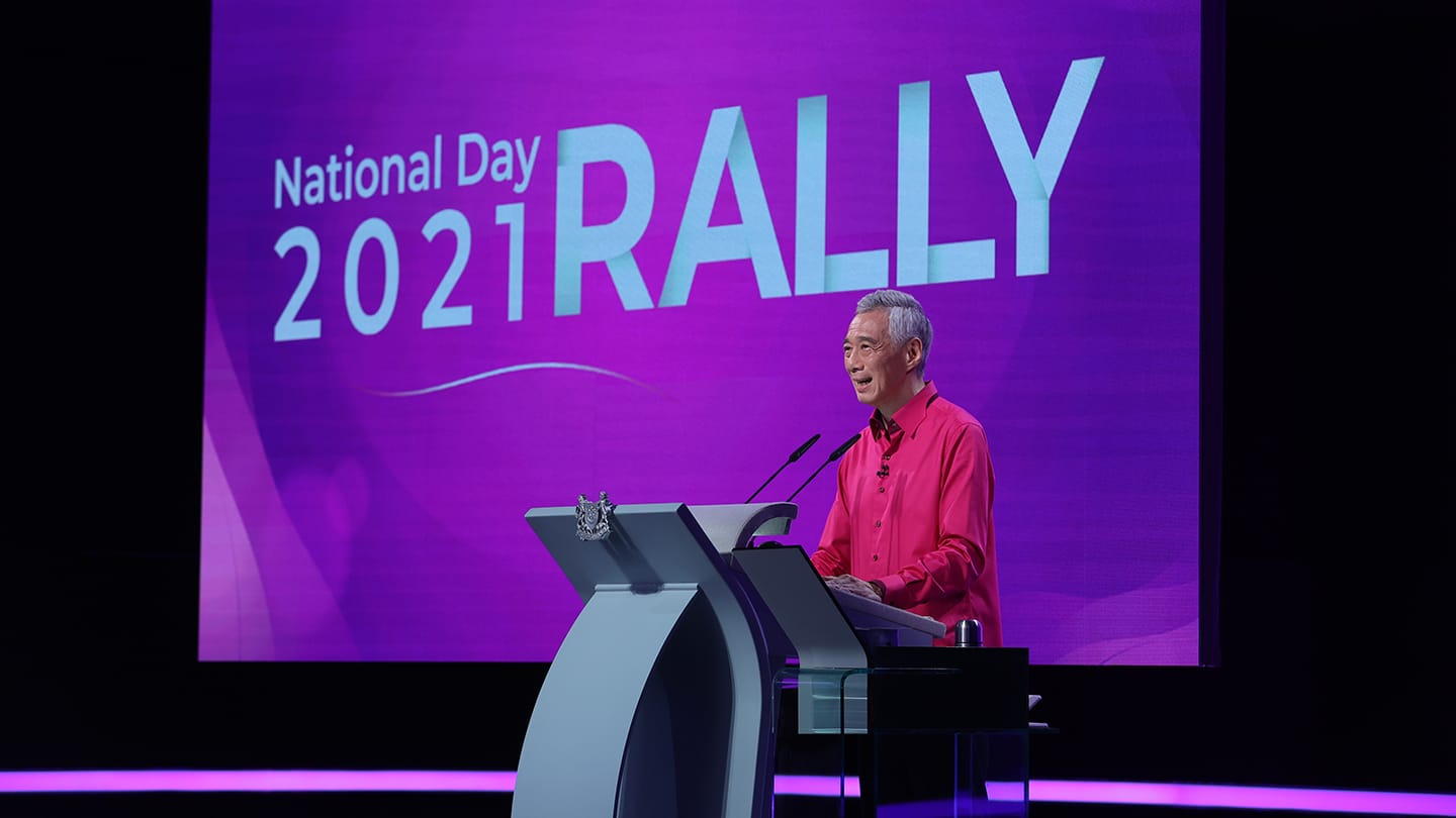 Lee Hsien Loong at podium, "National Day 2021 Rally" text in background.